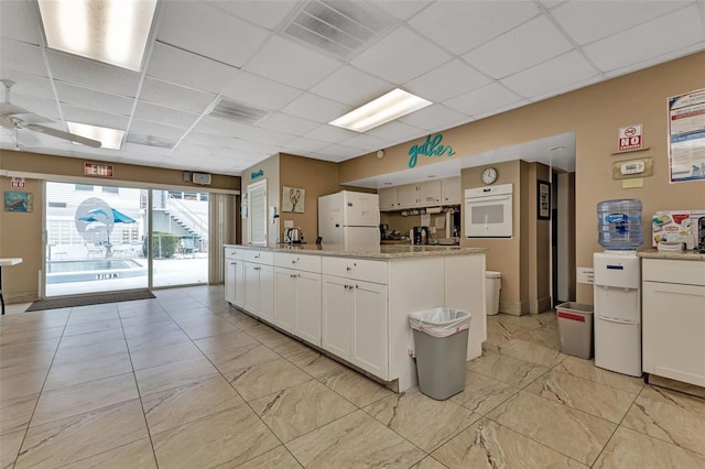 kitchen with white appliances, visible vents, a drop ceiling, and white cabinetry