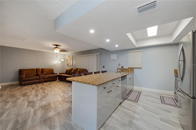 kitchen with appliances with stainless steel finishes, kitchen peninsula, sink, light stone counters, and white cabinets