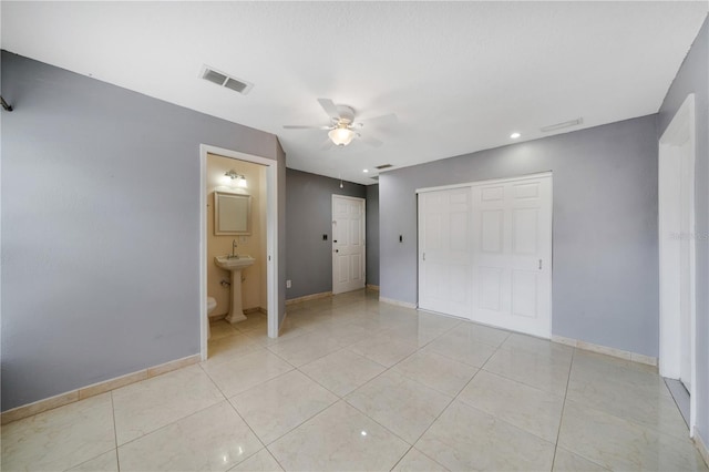 unfurnished bedroom with light tile patterned floors, a closet, ensuite bath, sink, and ceiling fan