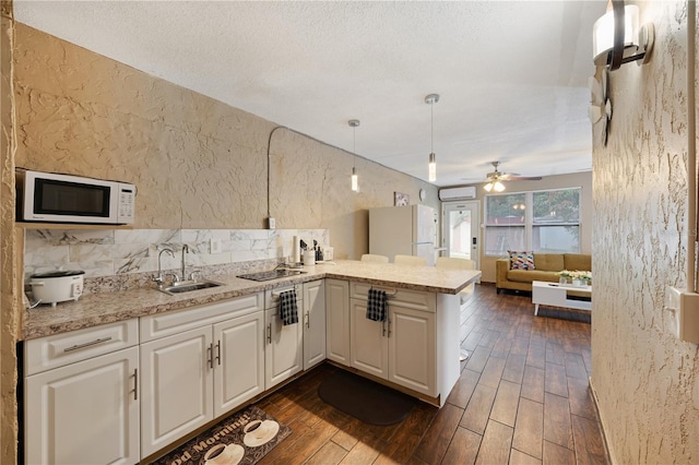 kitchen with white appliances, kitchen peninsula, ceiling fan, and dark hardwood / wood-style floors