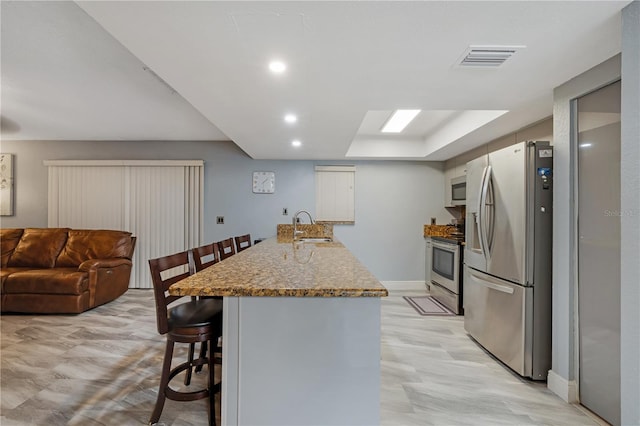 kitchen featuring light wood-type flooring, light stone countertops, stainless steel appliances, sink, and a kitchen breakfast bar