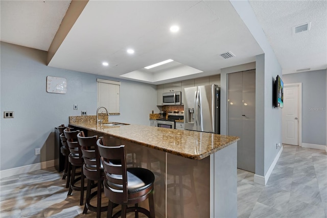 kitchen with stainless steel appliances, kitchen peninsula, light stone counters, sink, and a breakfast bar area