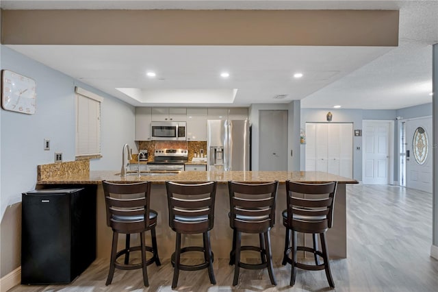 kitchen with a kitchen breakfast bar, appliances with stainless steel finishes, light hardwood / wood-style floors, kitchen peninsula, and light stone counters