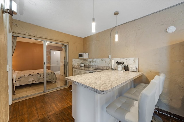 kitchen with hanging light fixtures, light brown cabinets, kitchen peninsula, dark wood-type flooring, and a breakfast bar