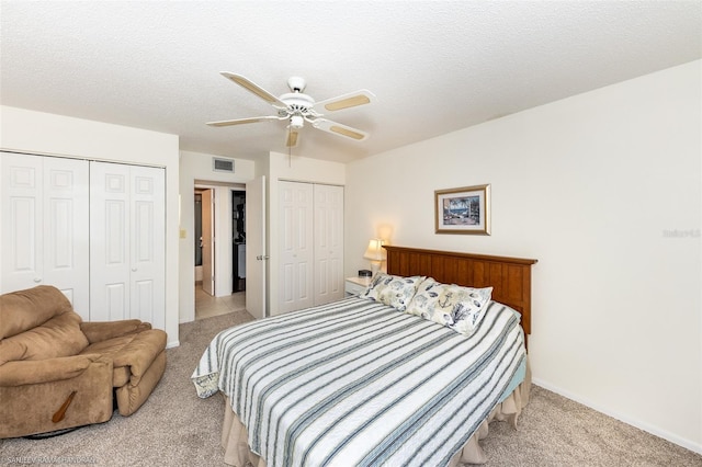 bedroom featuring ceiling fan, a textured ceiling, light carpet, and multiple closets