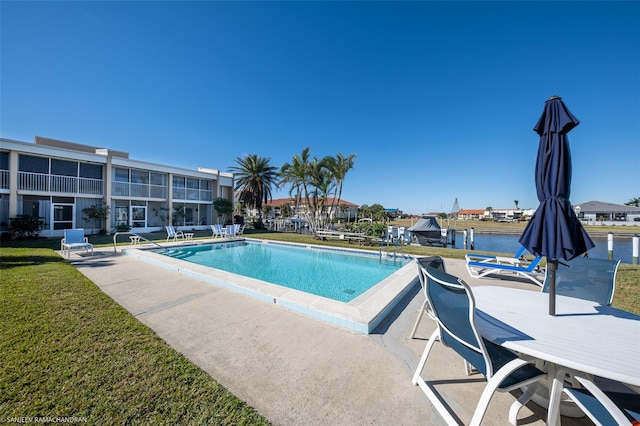 view of swimming pool with a patio area, a lawn, and a water view