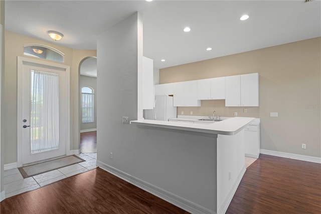 kitchen featuring sink, white cabinetry, wood-type flooring, kitchen peninsula, and white fridge