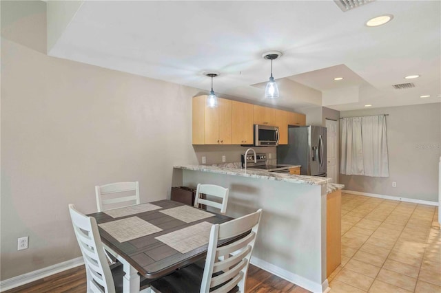 kitchen featuring hanging light fixtures, stainless steel appliances, light stone counters, kitchen peninsula, and light brown cabinets