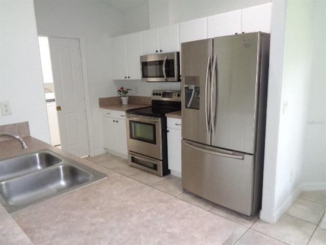 kitchen with washer / clothes dryer, stainless steel appliances, sink, light tile patterned floors, and white cabinetry