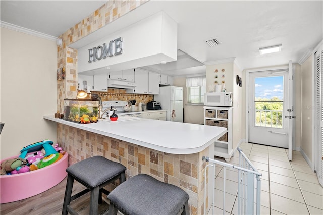 kitchen with white appliances, a breakfast bar, kitchen peninsula, crown molding, and white cabinetry