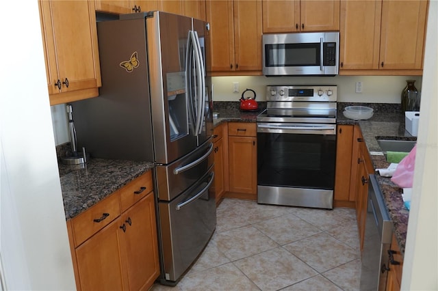 kitchen with dark stone countertops, stainless steel appliances, and light tile patterned floors