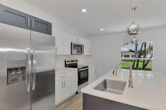 kitchen with tasteful backsplash, light wood-type flooring, appliances with stainless steel finishes, pendant lighting, and sink