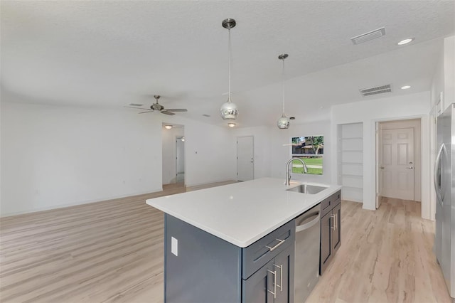 kitchen featuring light wood-type flooring, stainless steel appliances, decorative light fixtures, sink, and a kitchen island with sink