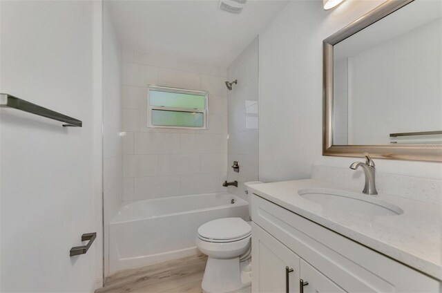 full bathroom with wood-type flooring, tiled shower / bath combo, vanity, and toilet