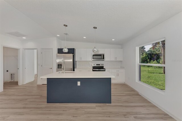 kitchen with a center island with sink, stainless steel appliances, white cabinets, pendant lighting, and vaulted ceiling