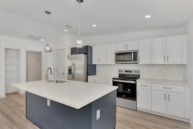 kitchen featuring stainless steel appliances, decorative light fixtures, sink, white cabinetry, and a kitchen island with sink