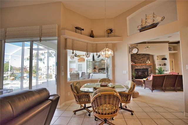 tiled dining area featuring a towering ceiling, a fireplace, built in features, and ceiling fan with notable chandelier