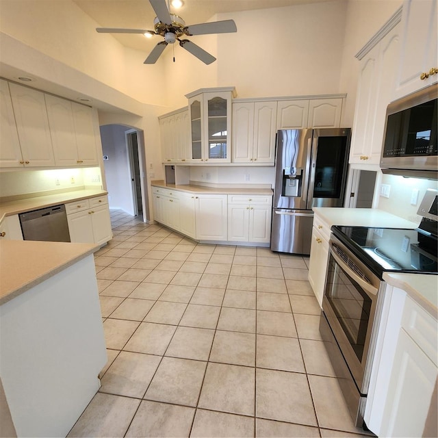 kitchen with white cabinets, a towering ceiling, appliances with stainless steel finishes, and light tile patterned floors