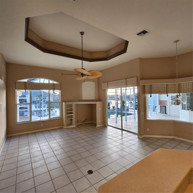 interior space with a wealth of natural light, ceiling fan, light tile patterned floors, and a raised ceiling