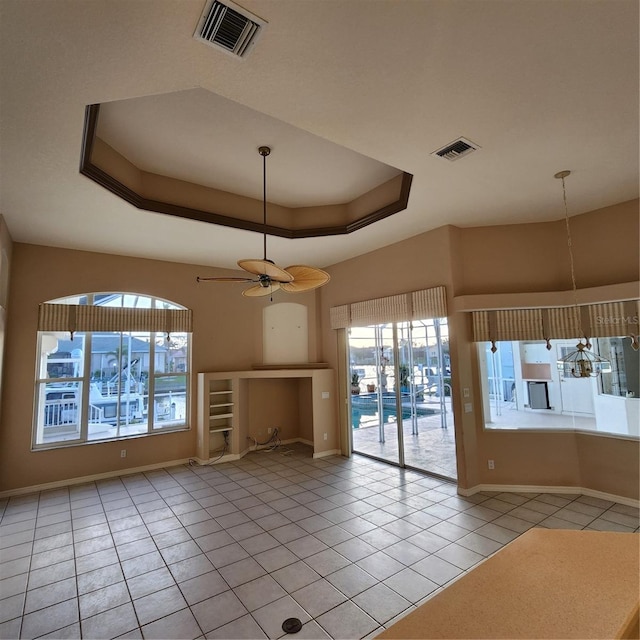 interior space with a raised ceiling, light tile patterned floors, and ceiling fan