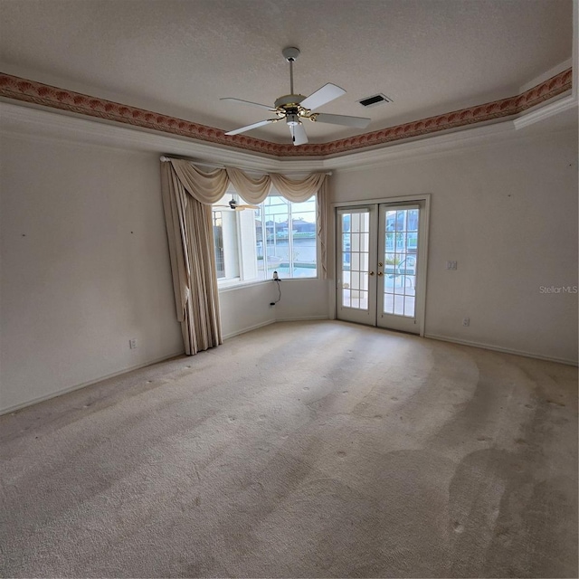 carpeted spare room featuring a water view, ceiling fan, a textured ceiling, a tray ceiling, and french doors