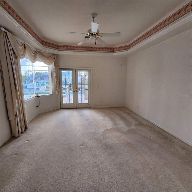 carpeted spare room featuring french doors, a textured ceiling, ornamental molding, ceiling fan, and a raised ceiling