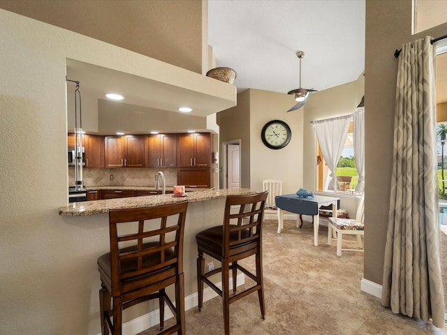 kitchen with sink, a breakfast bar area, backsplash, kitchen peninsula, and light stone countertops