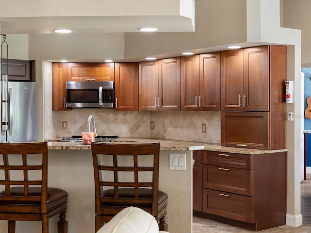 kitchen with stainless steel appliances, light stone counters, a kitchen breakfast bar, and decorative backsplash