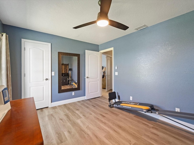 workout room with ceiling fan, light hardwood / wood-style floors, and a textured ceiling