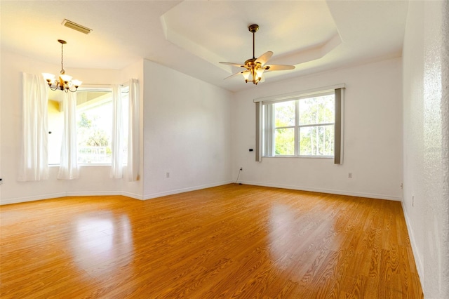 empty room featuring hardwood / wood-style flooring, plenty of natural light, ceiling fan with notable chandelier, and a tray ceiling