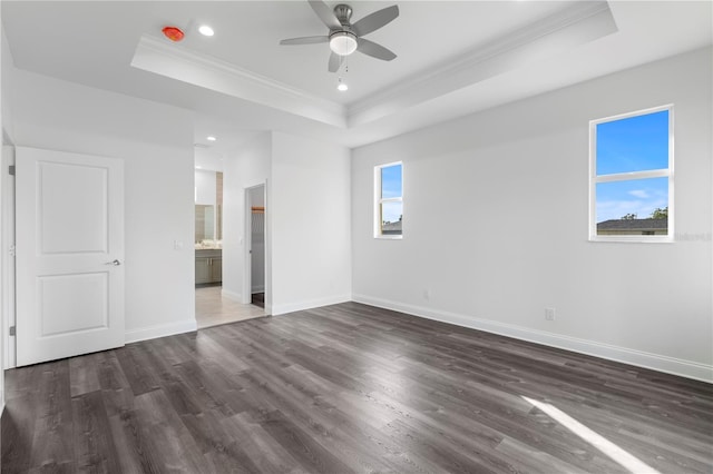 unfurnished bedroom with baseboards, a tray ceiling, dark wood finished floors, and crown molding