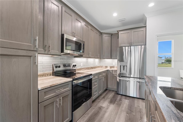 kitchen with stainless steel appliances, light stone countertops, backsplash, ornamental molding, and wood finished floors