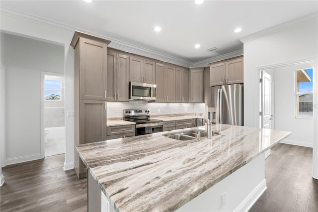 kitchen with stainless steel appliances, a sink, light stone counters, and a spacious island