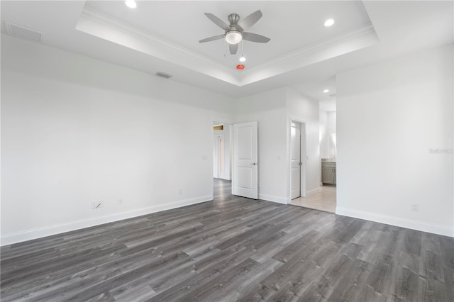 unfurnished room featuring a tray ceiling, dark wood finished floors, visible vents, ornamental molding, and baseboards