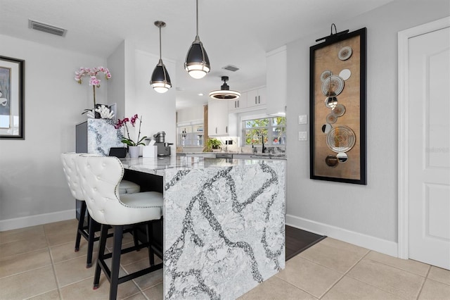 kitchen with white cabinetry, a breakfast bar, light stone counters, and light tile patterned floors