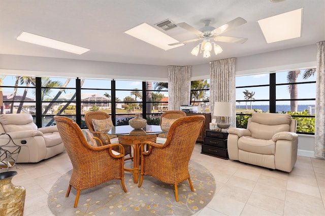 tiled dining area featuring a skylight, a water view, ceiling fan, and a healthy amount of sunlight