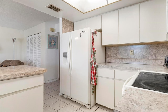 kitchen with white cabinetry, white fridge with ice dispenser, a textured ceiling, and light tile patterned flooring