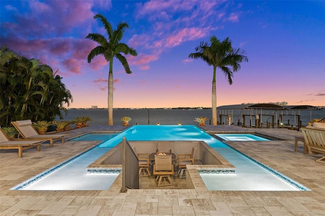 pool at dusk featuring a patio and a pool with connected hot tub