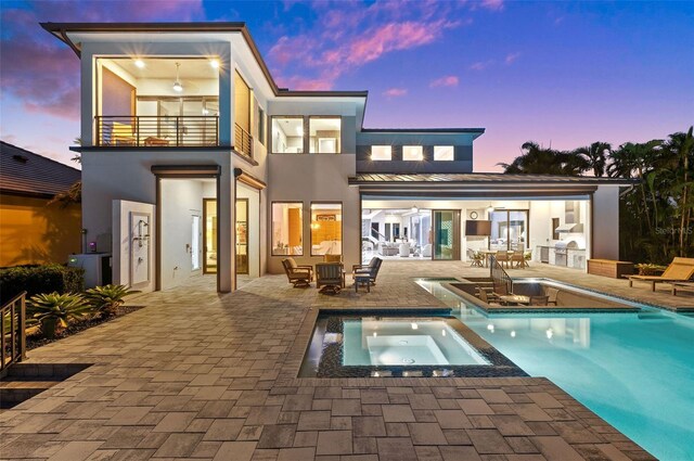 back of house at dusk featuring a patio, a balcony, a pool with connected hot tub, and stucco siding