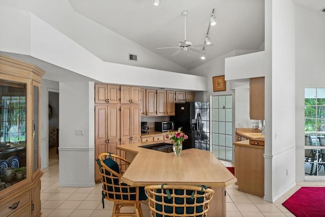 kitchen with high vaulted ceiling, light tile patterned floors, and black fridge