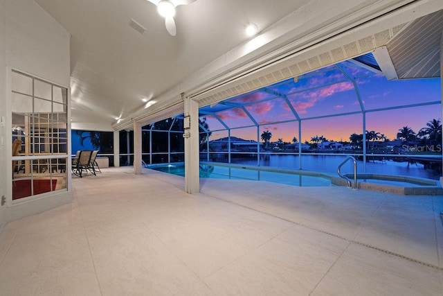 pool at dusk featuring an in ground hot tub, glass enclosure, a water view, and a patio