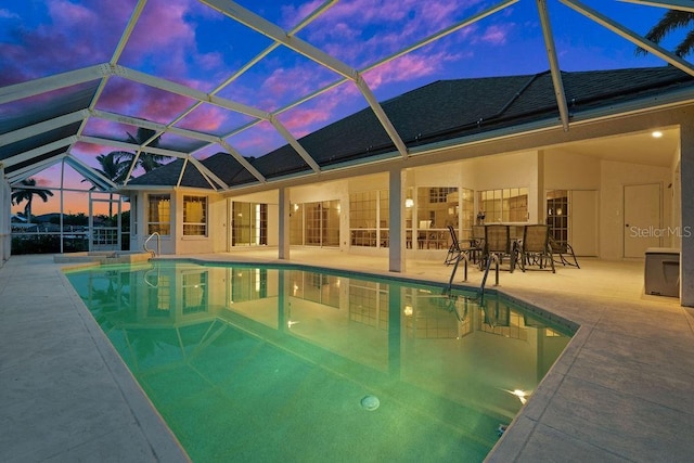 pool at dusk with glass enclosure and a patio area