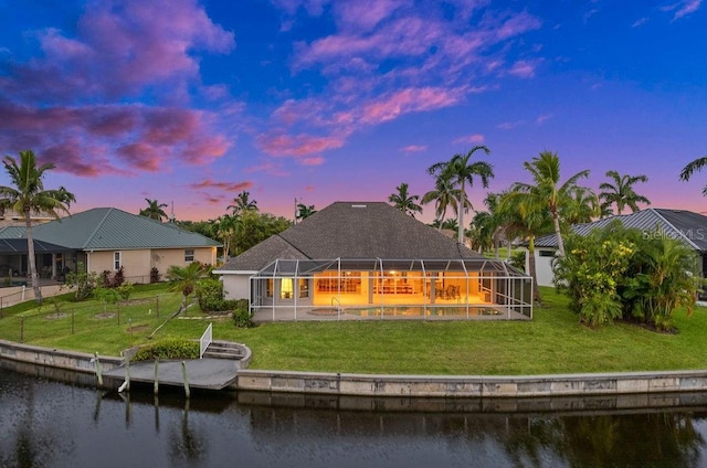 back house at dusk with a lanai, a lawn, and a water view