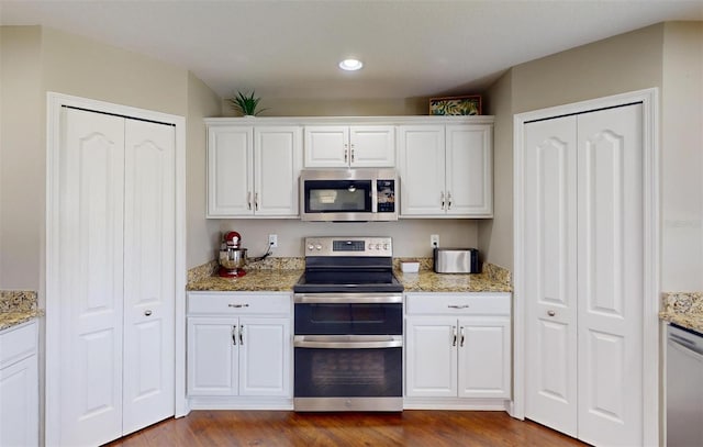 kitchen with dark wood-type flooring, stainless steel appliances, light stone counters, and white cabinets