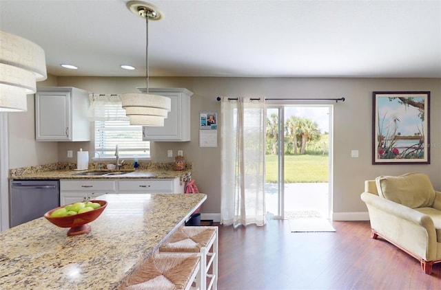 kitchen with decorative light fixtures, sink, white cabinets, stainless steel dishwasher, and light stone counters