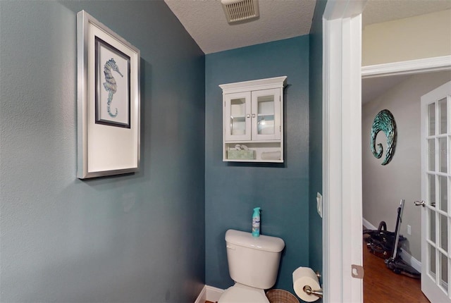 bathroom featuring hardwood / wood-style flooring, toilet, french doors, and a textured ceiling