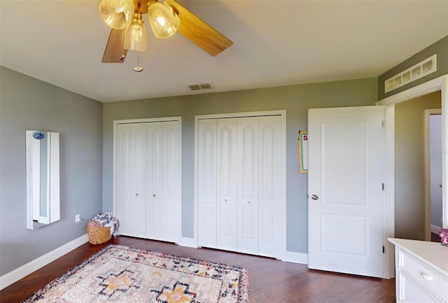 bedroom with dark hardwood / wood-style floors, two closets, and ceiling fan