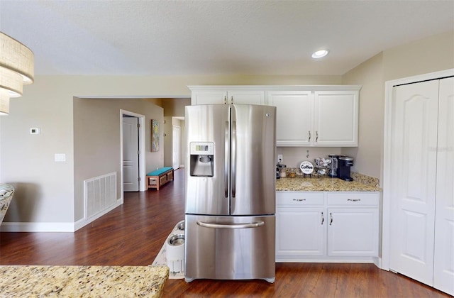 kitchen featuring light stone counters, dark wood-type flooring, stainless steel fridge, and white cabinets