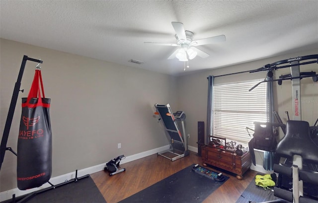 workout room with ceiling fan, dark wood-type flooring, and a textured ceiling