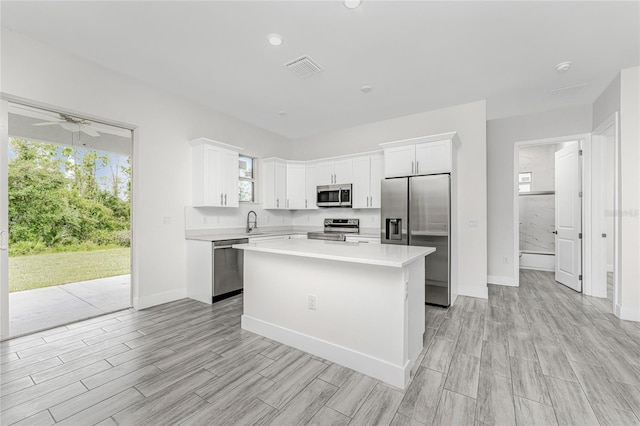 kitchen featuring sink, ceiling fan, stainless steel appliances, white cabinets, and a kitchen island